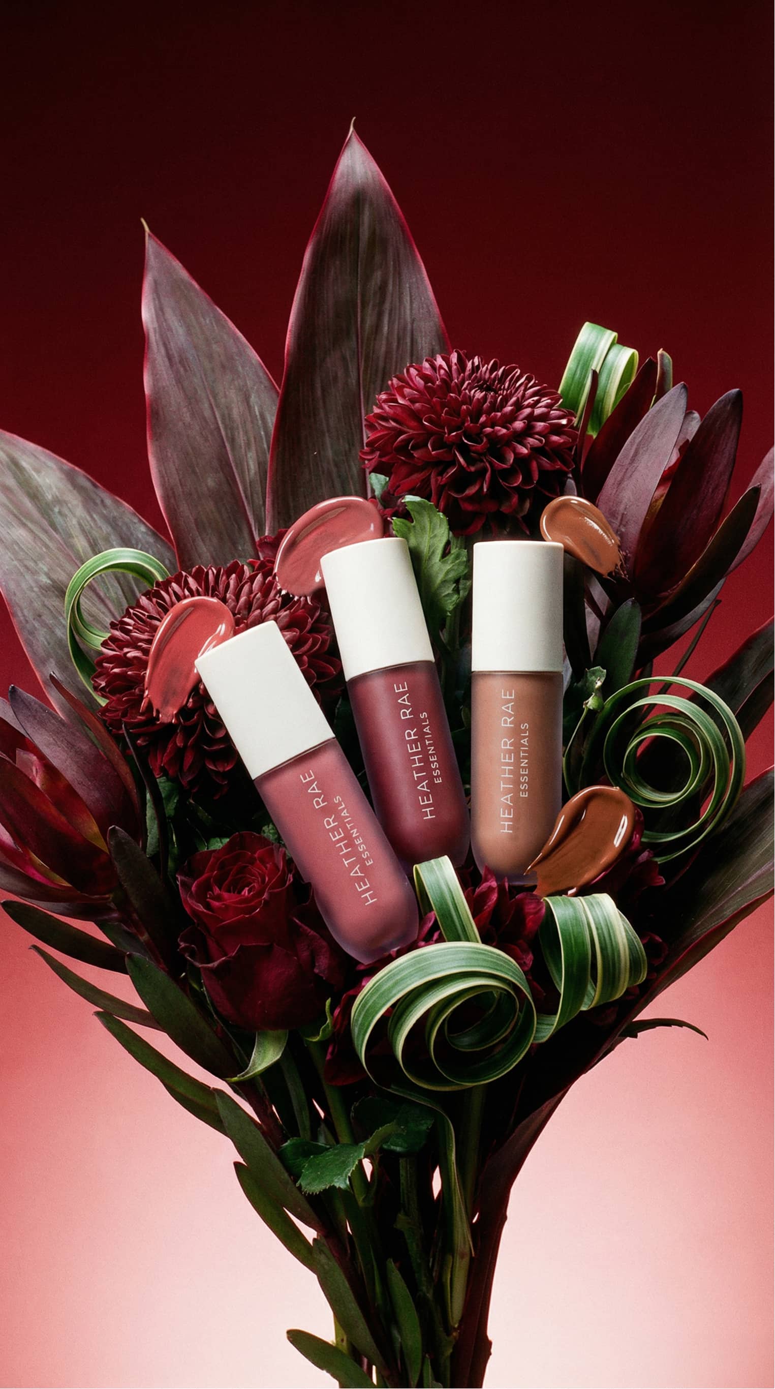 Deep red botanical and product composition with lip gloss collection, velvet crimson petals, and cosmetic swatch smears