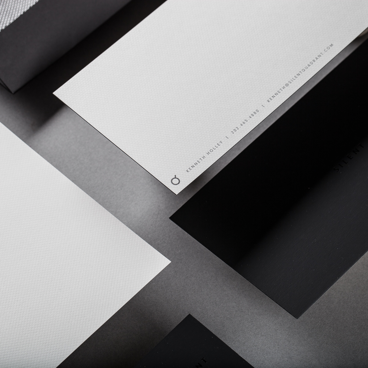 Angled tactile detail of textured cream stationery with minimal Q mark overlapping matte black folder