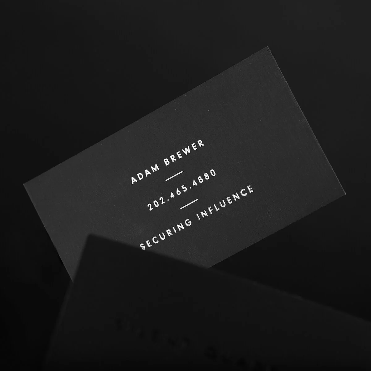 Reverse of Silent Quadrant business card: Adam Brewer, Securing Influence in silver foil on matte black