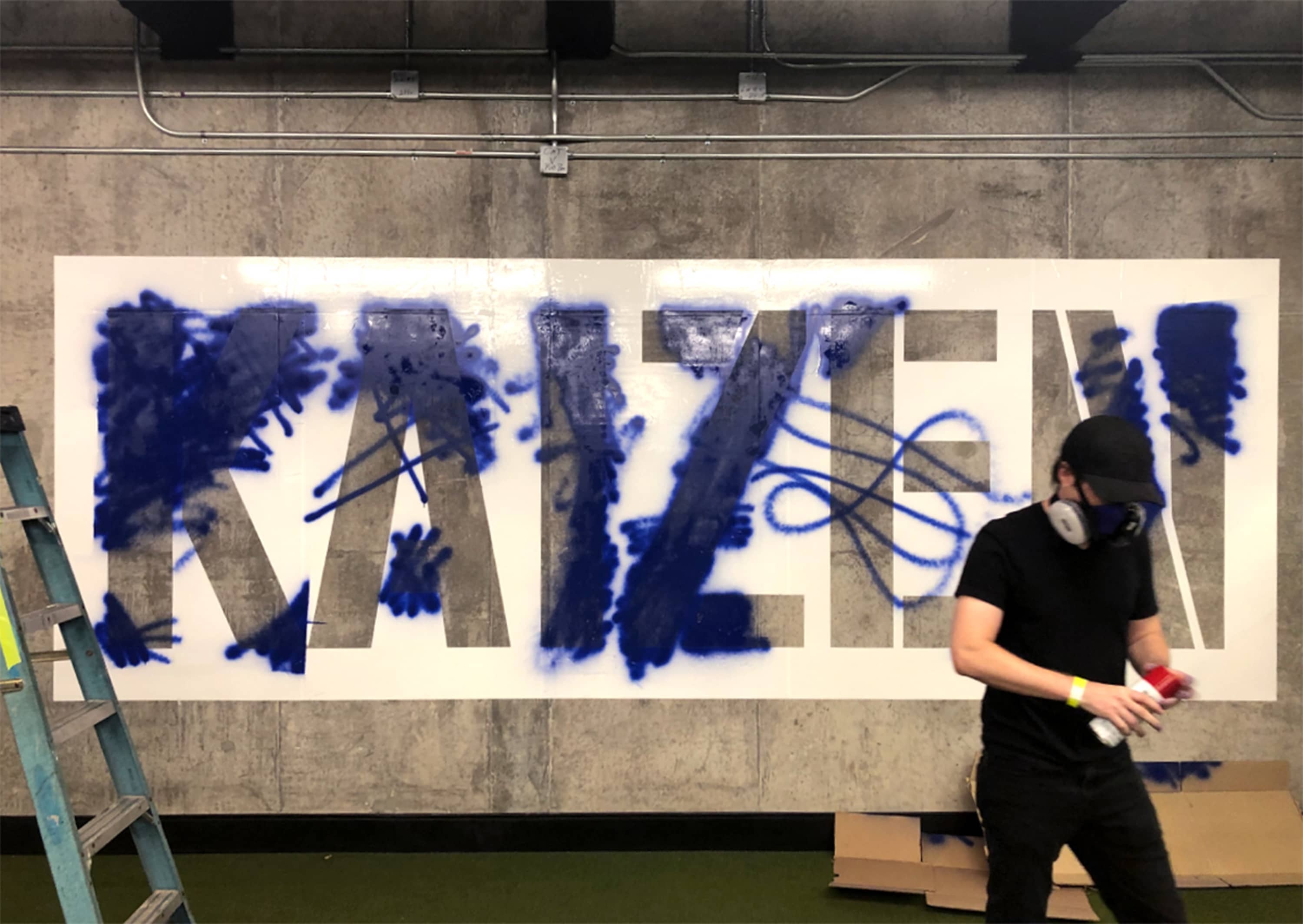 Installer applying spray paint through laser-cut stencil on raw concrete